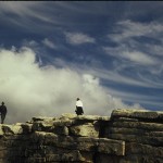 Two people standing on a rock wall looking at the sky.